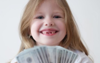 little girl smiling while holding handful of $100 bills