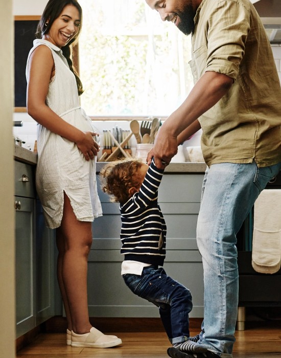 father swinging child by arms in kitchen playfully while mother watches and smiles
