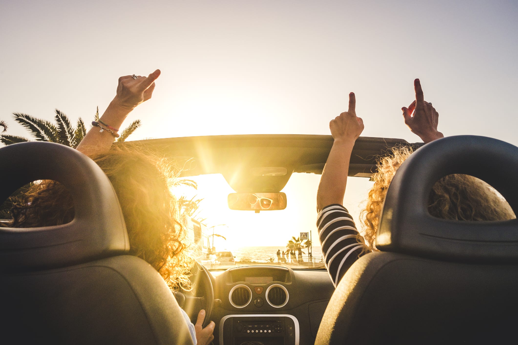 Couple of woman friends traveling and driving having a lot of fun dancing in the car with opened roof and summer vacation sunset ocean in front – concept of friendship together and nice lifestyle for independent girls