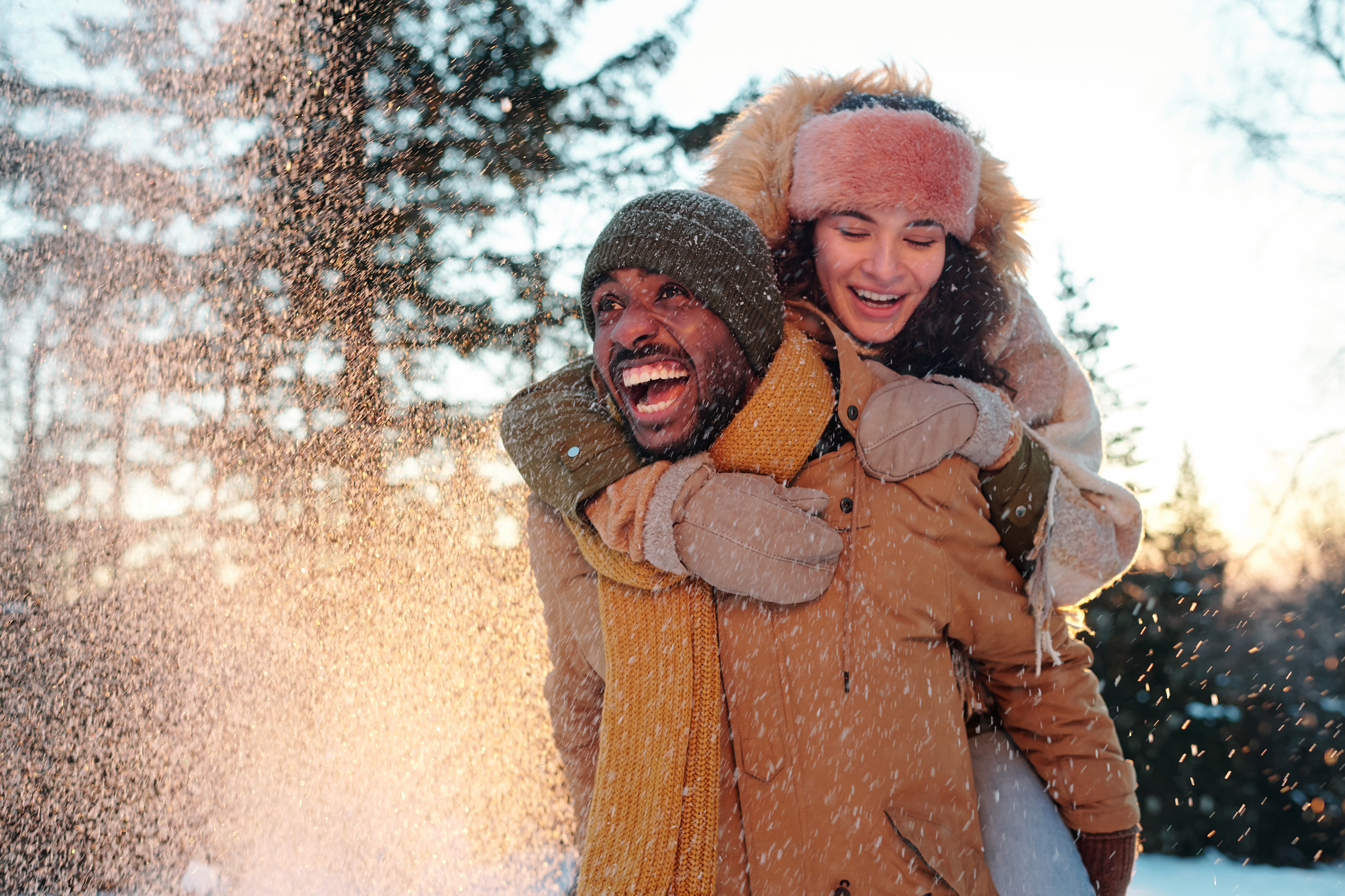 Cheerful multiracial couple in winterwear laughing while girl embracing her boyfriend