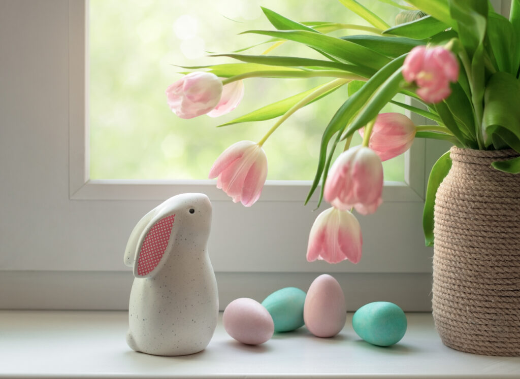 Ceramic Easter bunny, colorful dyed eggs and tulip flowers on windowsill. Decorations for Easter celebration at home