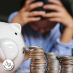 man with head in hands behind piggy bank and coins
